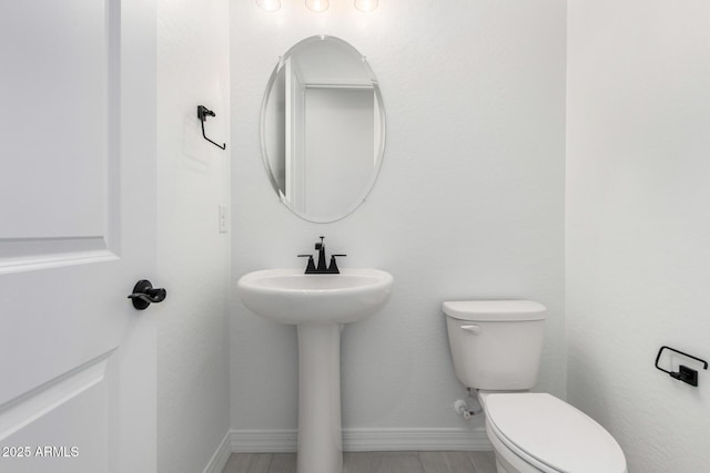 half bath featuring baseboards and toilet