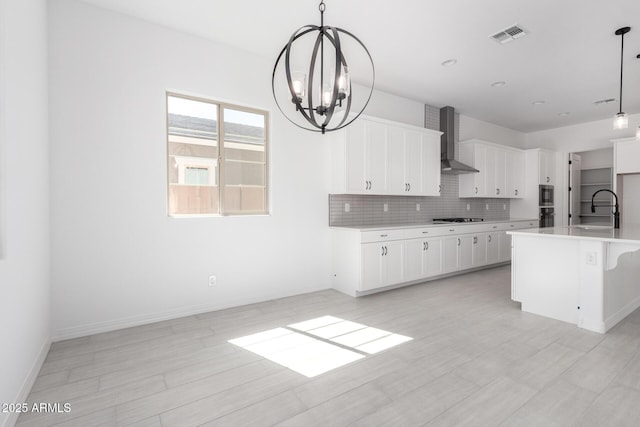kitchen with an inviting chandelier, decorative backsplash, stainless steel appliances, wall chimney range hood, and a sink