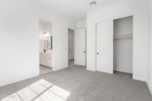 unfurnished bedroom featuring ensuite bath, a closet, light carpet, baseboards, and visible vents