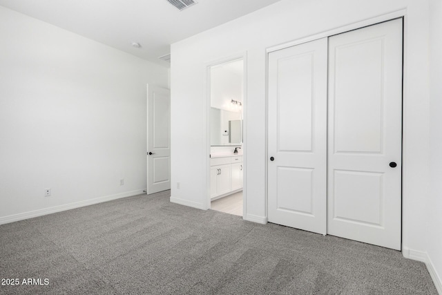 unfurnished bedroom featuring a closet, visible vents, light carpet, baseboards, and ensuite bathroom