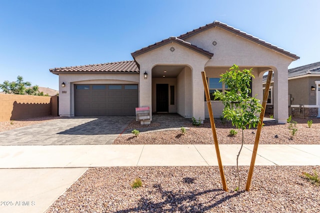 mediterranean / spanish home featuring a garage, stucco siding, decorative driveway, and a tiled roof
