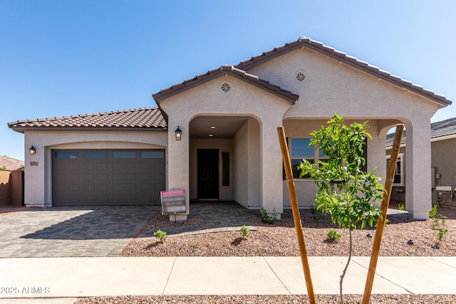 mediterranean / spanish home featuring stucco siding, a tile roof, decorative driveway, and an attached garage
