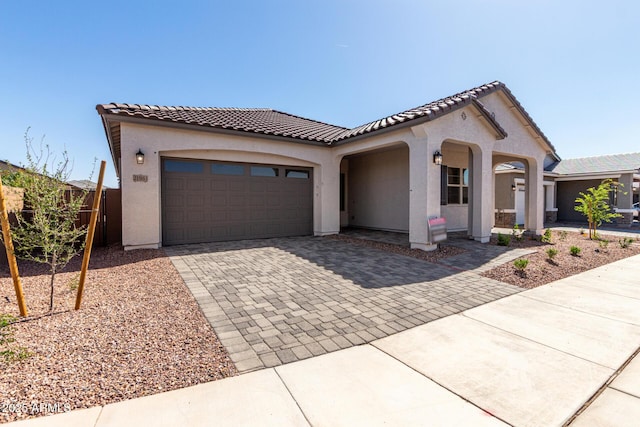 mediterranean / spanish house featuring an attached garage, a tile roof, decorative driveway, and stucco siding
