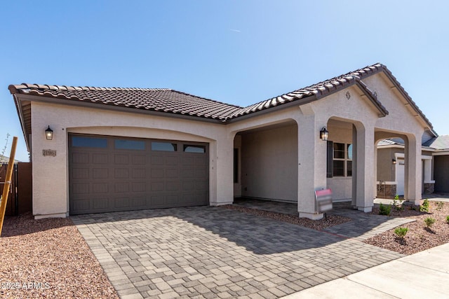 mediterranean / spanish-style home with decorative driveway, stucco siding, a tiled roof, and a garage