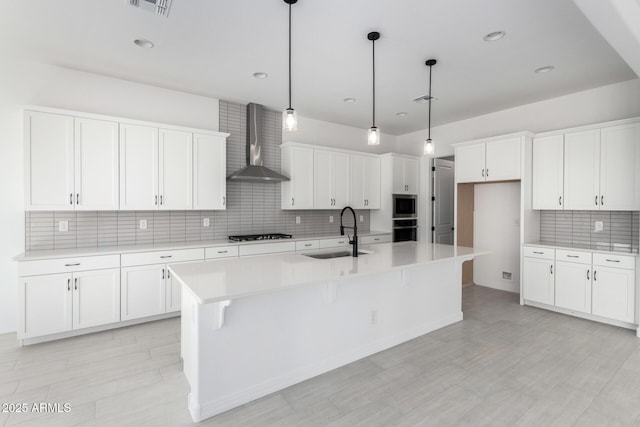 kitchen featuring tasteful backsplash, a sink, wall oven, gas stovetop, and wall chimney exhaust hood