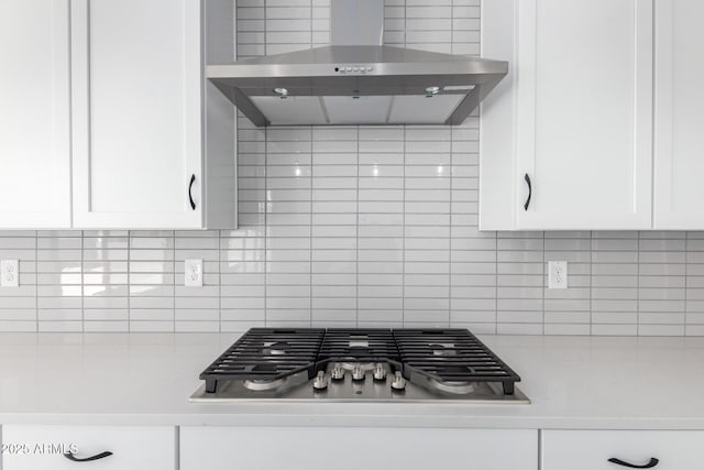 kitchen featuring wall chimney range hood, white cabinetry, stainless steel gas stovetop, light countertops, and backsplash