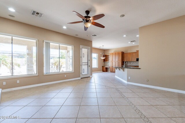 unfurnished living room featuring light tile patterned flooring, sink, and ceiling fan