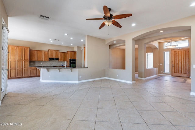 kitchen with light tile patterned floors, black fridge, ceiling fan, tasteful backsplash, and a breakfast bar