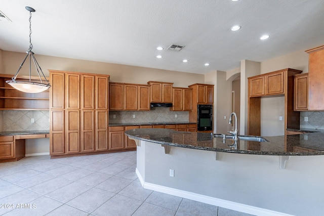 kitchen featuring a breakfast bar area, dark stone countertops, tasteful backsplash, and sink