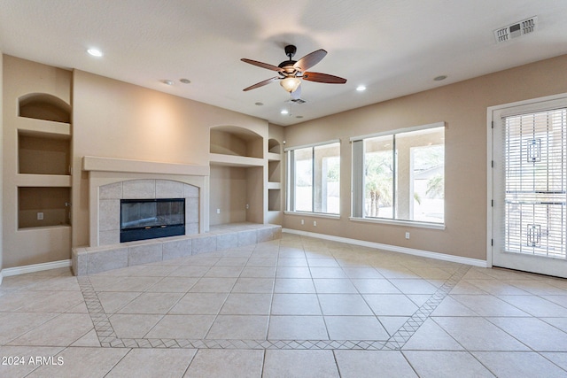 unfurnished living room featuring a textured ceiling, a tiled fireplace, built in shelves, ceiling fan, and light tile patterned flooring