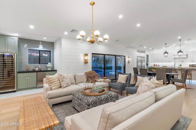 living room featuring lofted ceiling, wet bar, a chandelier, and light hardwood / wood-style flooring