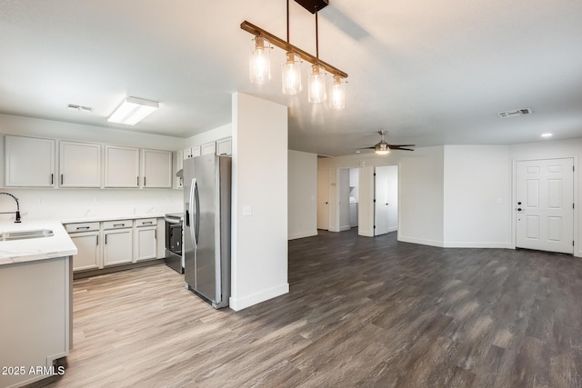 kitchen with stainless steel appliances, visible vents, a sink, wood finished floors, and baseboards