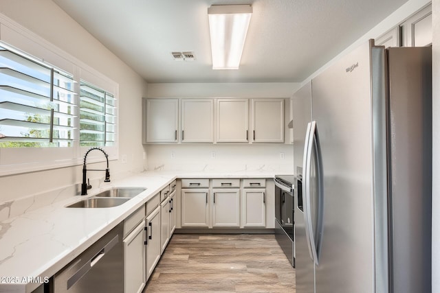 kitchen with visible vents, light wood-style flooring, light stone countertops, stainless steel appliances, and a sink