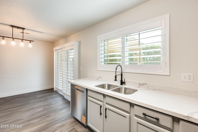 kitchen featuring light stone counters, decorative light fixtures, a sink, light wood-type flooring, and stainless steel dishwasher