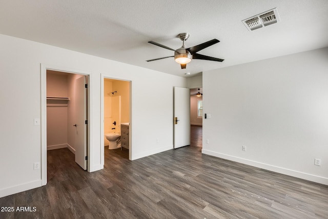 unfurnished bedroom with baseboards, wood finished floors, visible vents, and a walk in closet