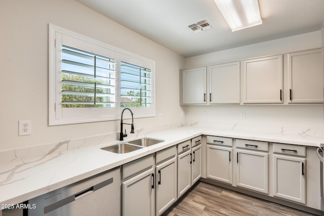 kitchen with light stone counters, a sink, visible vents, light wood-style floors, and stainless steel dishwasher