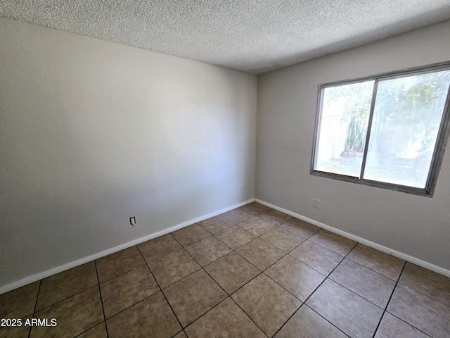 spare room with a textured ceiling, tile patterned flooring, and baseboards