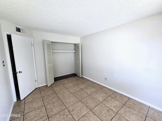 unfurnished bedroom with visible vents, light tile patterned floors, a closet, baseboards, and a textured ceiling