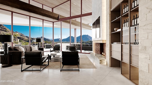 tiled living room featuring a stone fireplace, built in features, a mountain view, a wall of windows, and a high ceiling