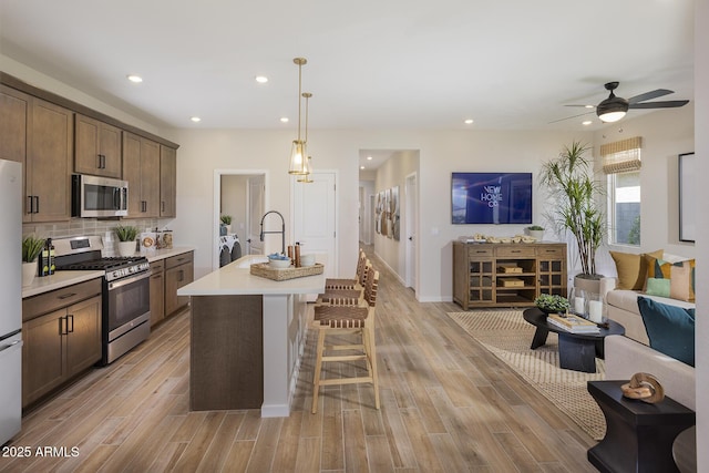 kitchen featuring appliances with stainless steel finishes, washer and dryer, a center island with sink, hanging light fixtures, and a breakfast bar area