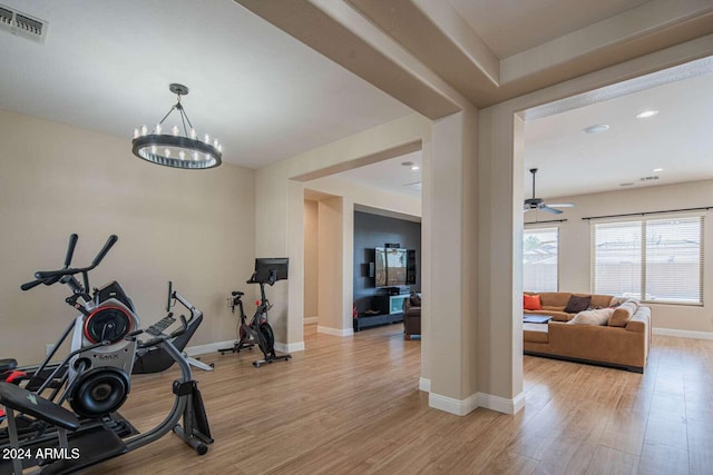 exercise area featuring ceiling fan with notable chandelier and light wood-type flooring