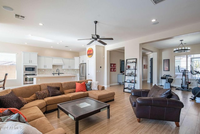 living room featuring ceiling fan with notable chandelier, light hardwood / wood-style floors, and sink