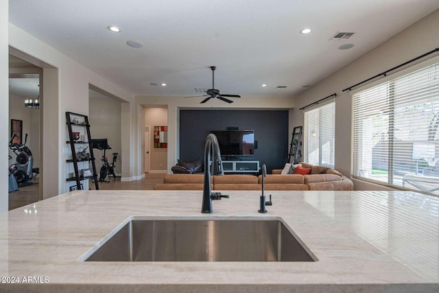 kitchen featuring light stone countertops, ceiling fan with notable chandelier, and sink