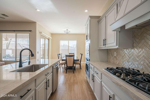 kitchen featuring sink, light hardwood / wood-style flooring, decorative backsplash, light stone countertops, and stainless steel appliances