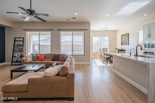 living room with plenty of natural light, sink, ceiling fan with notable chandelier, and light hardwood / wood-style flooring