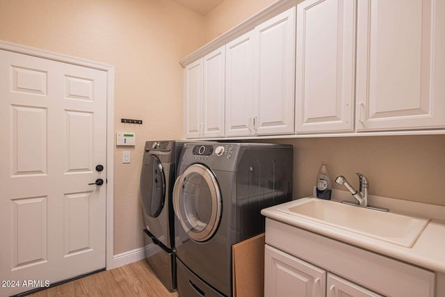 laundry room with washing machine and dryer, sink, cabinets, and light hardwood / wood-style flooring