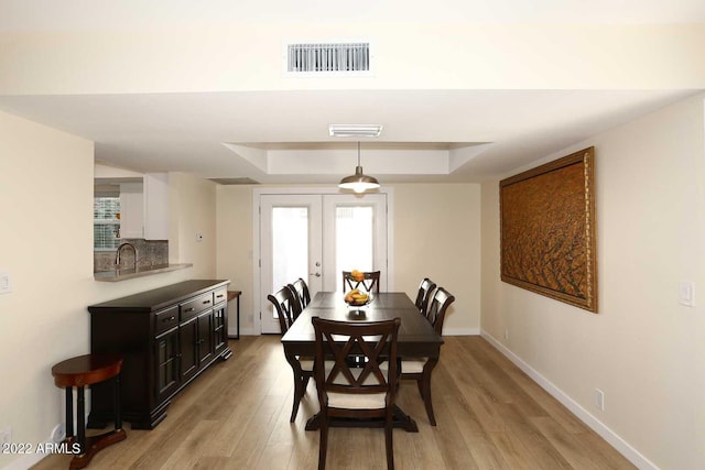 dining area featuring a raised ceiling, light hardwood / wood-style flooring, and french doors