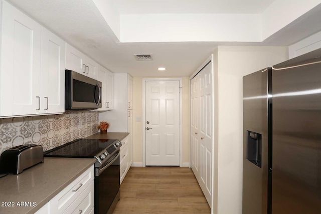 kitchen featuring white cabinets, decorative backsplash, appliances with stainless steel finishes, and light hardwood / wood-style flooring