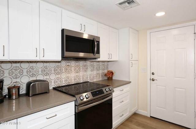 kitchen with light wood-type flooring, white cabinetry, backsplash, and appliances with stainless steel finishes