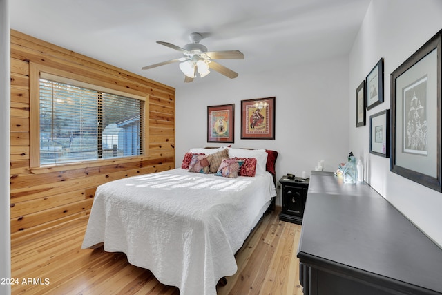 bedroom with light hardwood / wood-style floors, wood walls, and ceiling fan