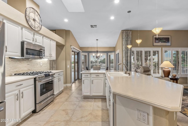 kitchen featuring stainless steel appliances, an island with sink, decorative backsplash, and white cabinets