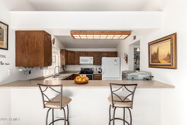 kitchen with kitchen peninsula, a kitchen bar, sink, and white appliances