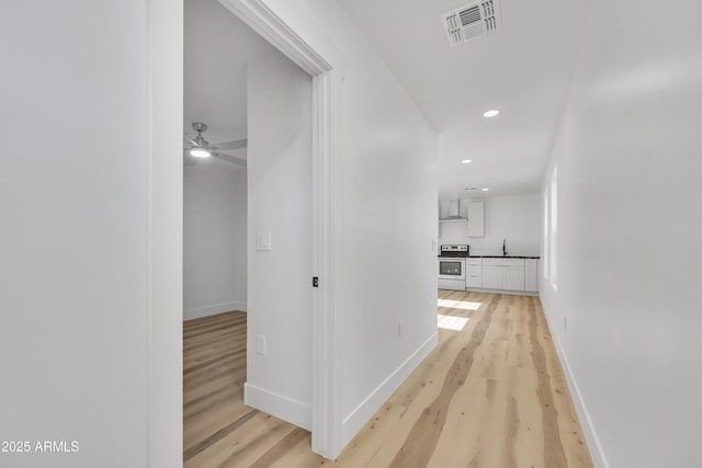 hallway featuring baseboards, visible vents, recessed lighting, a sink, and light wood-type flooring