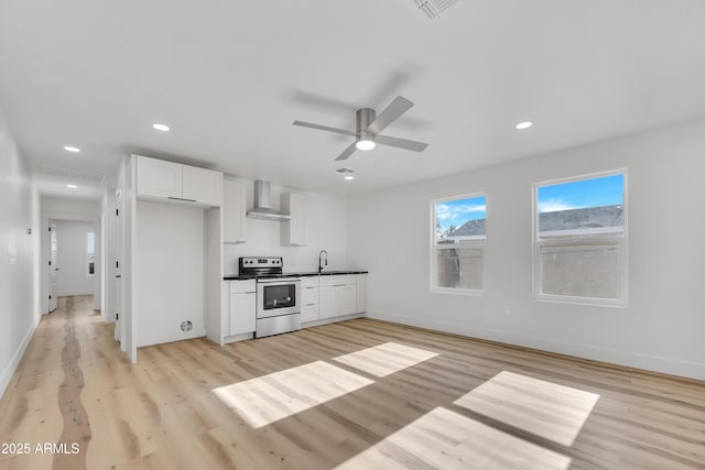 kitchen featuring stainless steel electric range oven, a ceiling fan, white cabinetry, wall chimney exhaust hood, and light wood-type flooring