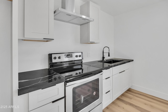 kitchen featuring electric range, a sink, dark countertops, white cabinetry, and wall chimney exhaust hood