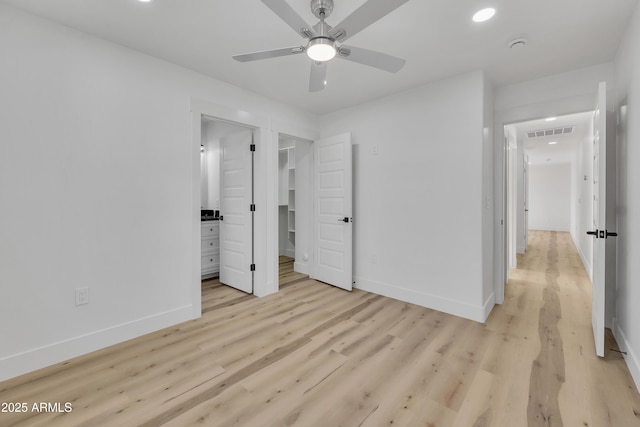 unfurnished bedroom with visible vents, light wood-style flooring, a walk in closet, and baseboards