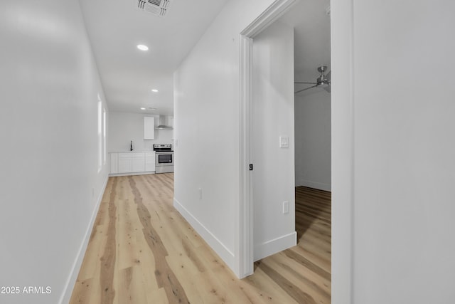 hallway featuring visible vents, light wood-style flooring, and baseboards