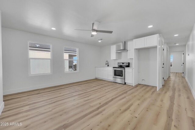 kitchen featuring light wood-type flooring, a sink, white cabinetry, wall chimney range hood, and stainless steel electric range oven