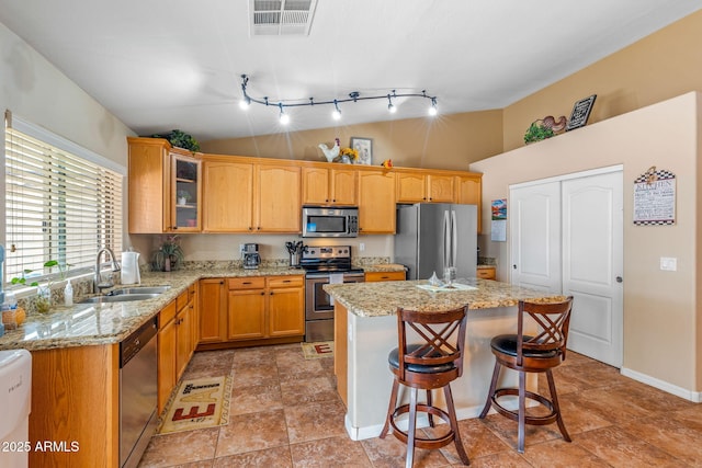 kitchen with visible vents, a sink, a kitchen island, appliances with stainless steel finishes, and glass insert cabinets