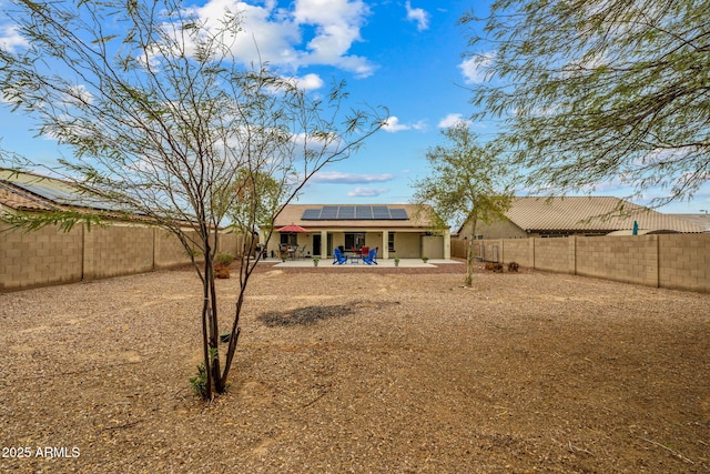 back of house featuring a fenced backyard, roof mounted solar panels, stucco siding, and a patio