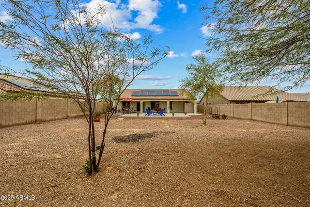 back of house featuring a fenced backyard, roof mounted solar panels, stucco siding, and a patio