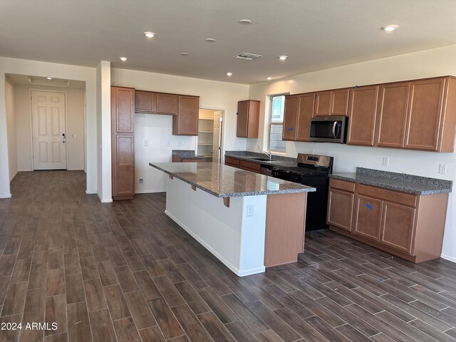 kitchen with dark stone counters, stainless steel appliances, a center island, visible vents, and dark wood finished floors