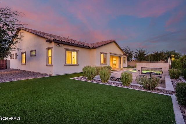 back house at dusk with a lawn and a patio