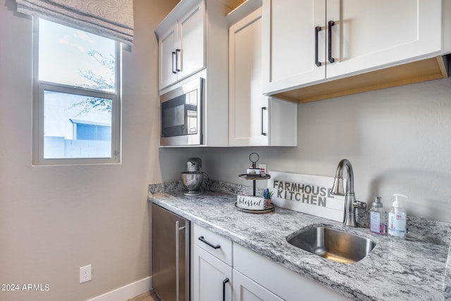 kitchen featuring light stone counters, stainless steel microwave, sink, and white cabinetry