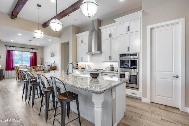 kitchen featuring appliances with stainless steel finishes, white cabinetry, an island with sink, wall chimney exhaust hood, and sink