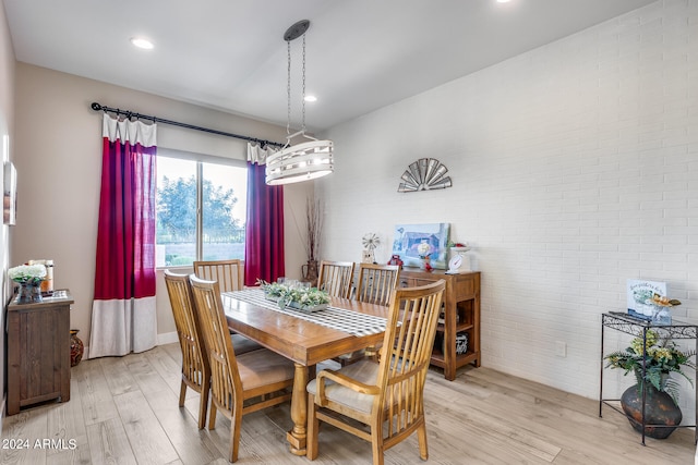 dining room featuring light wood-type flooring, a chandelier, and brick wall